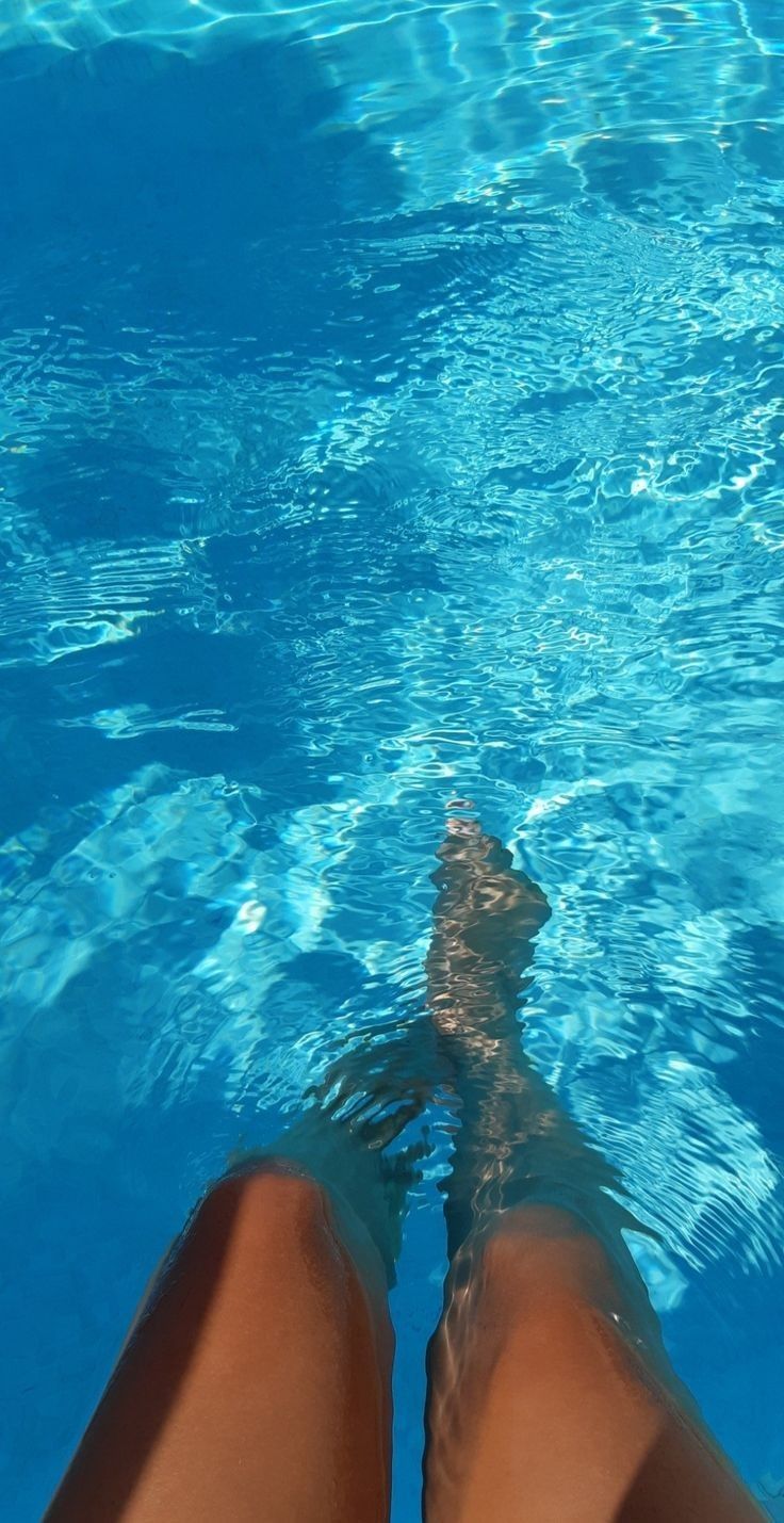 a person's legs in the water with their feet above the blue pool surface