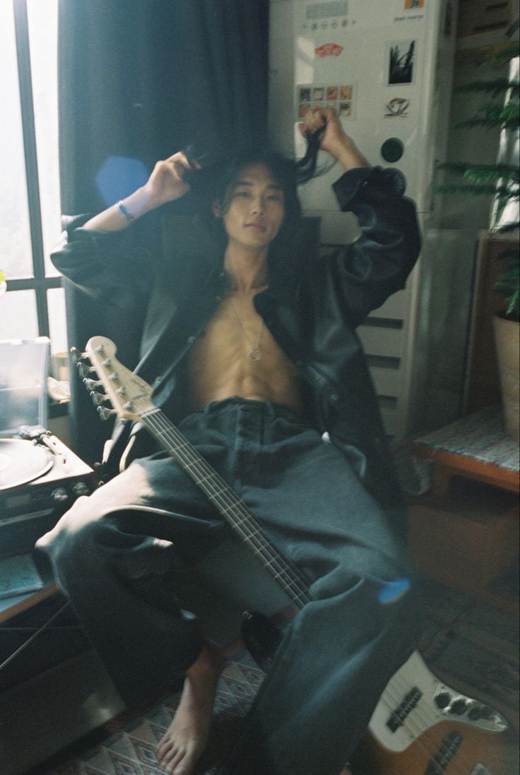 a shirtless man sitting on the floor with an electric guitar in his hand and looking at the camera