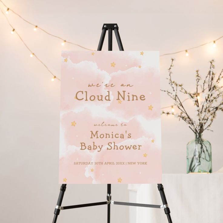 a baby shower sign sitting on top of a easel next to a vase filled with flowers