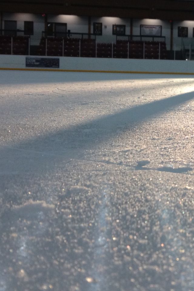 an ice skating rink with the sun shining on it's surface and lights in the background