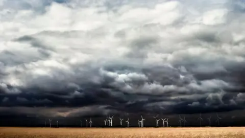 Wind turbines in the distance in front of a storm, grey and black sky full of clouds in Dungeness. 