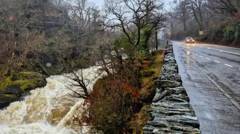 A flooded road to the right, and on the left a fast-flowing river 