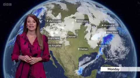 Elizabeth Rizzini in a red dress stands in front of a weather map of north America, showing snow storms in the east