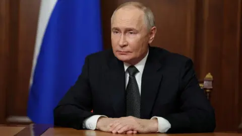 Russian President Vladimir Putin sits at his desk delivering an address to Russians on TV