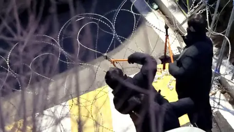 Police officers cut a wire fence set up at the entrance to the official residence of impeached South Korean President Yoon Suk Yeol, as authorities seek to execute an arrest warrant, in Seoul, South Korea, January 15, 2025.