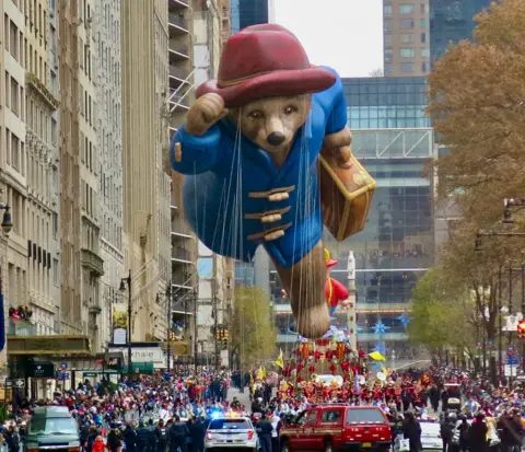 Roland Trope Large balloon of Paddington Bear is pulled down the road by a crowd on the ground