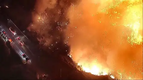 Aerial images of yellow wild fires flames near emergency vehicles on a road.