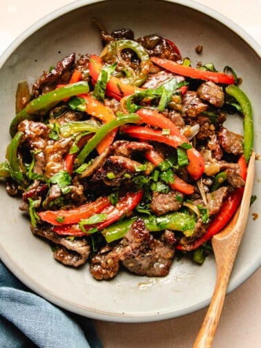 A close shot photo shows sliced and marinated beef stir fry with onions and peppers served in a light color plate.