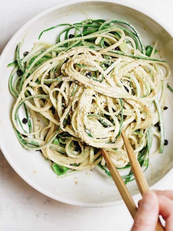 A close shot photo shows cucumber noodles drizzled with thai peanut sauce in a serving bowl