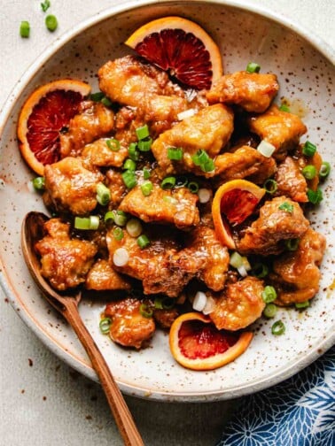 Photo shows homemade Panda express orange chicken served in a white plate with fresh slices of oranges.