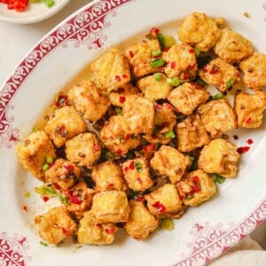 Photo shows air fryer salt and pepper tofu served on a white plate with salt pepper seasoning on the side.