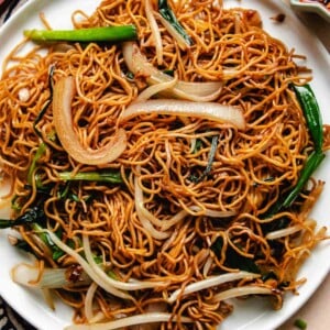 Feature image shows crispy Cantonese chow mein noodles with bean sprouts, onion, and garlic give served in a big white plate.