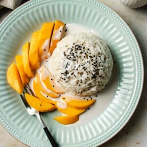 Feature image shows coconut sticky rice with mango served on a light blue color plate with sticky rice sauce.