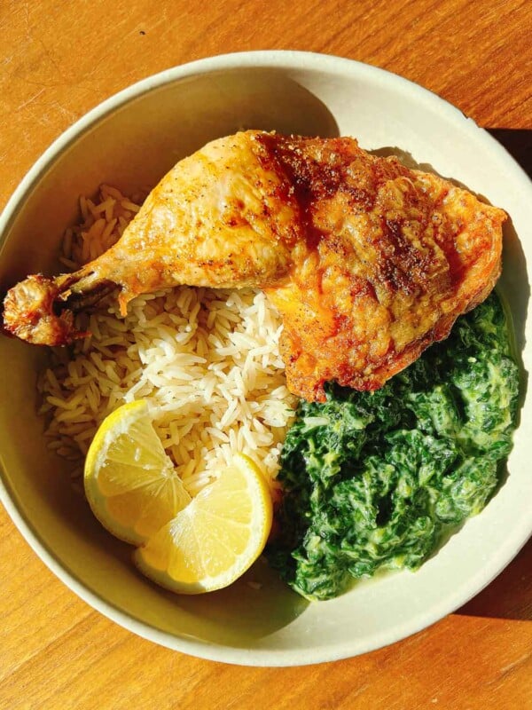 Feature image shows crispy air fryer chicken leg quarters served with rice and cream spinach in one plate.