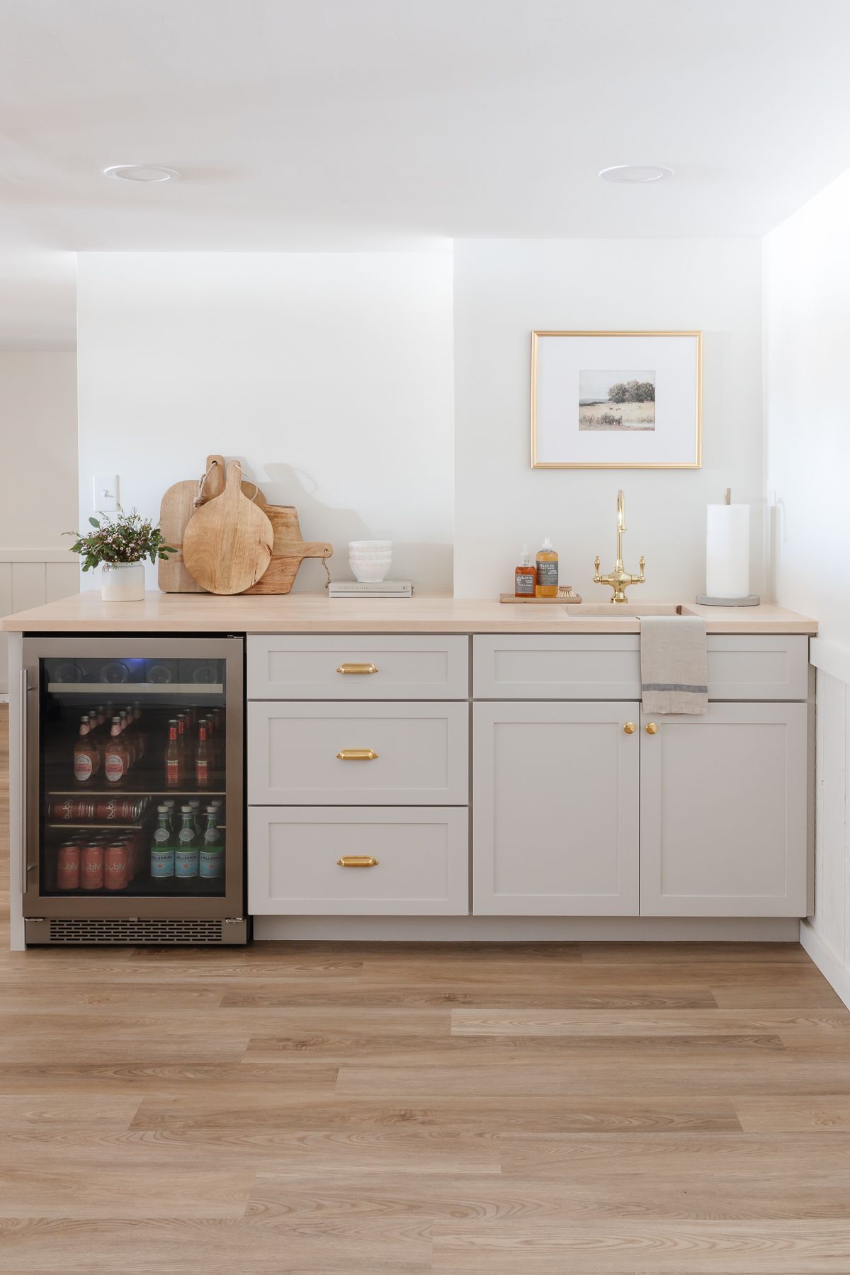 A small basement wet bar painted gray, beverage fridge to the left