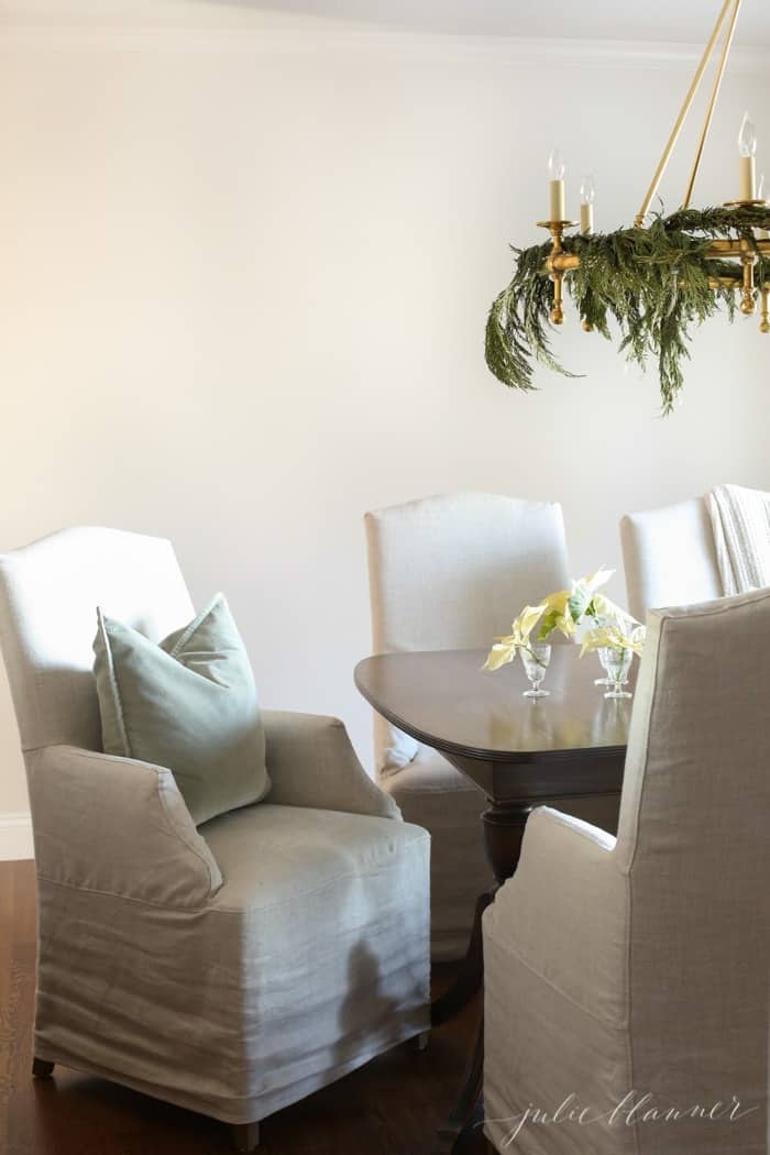 A round brass chandelier over a formal dining table with linen chairs, decorated for the holidays.