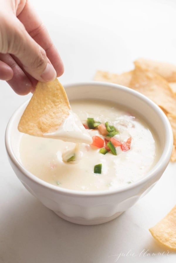 tortilla chip dipped in queso blanco dip in a white bowl