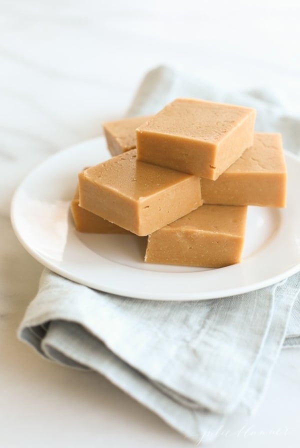 A stack of peanut butter fudge on a white plate, sitting atop a blue linen towel. .