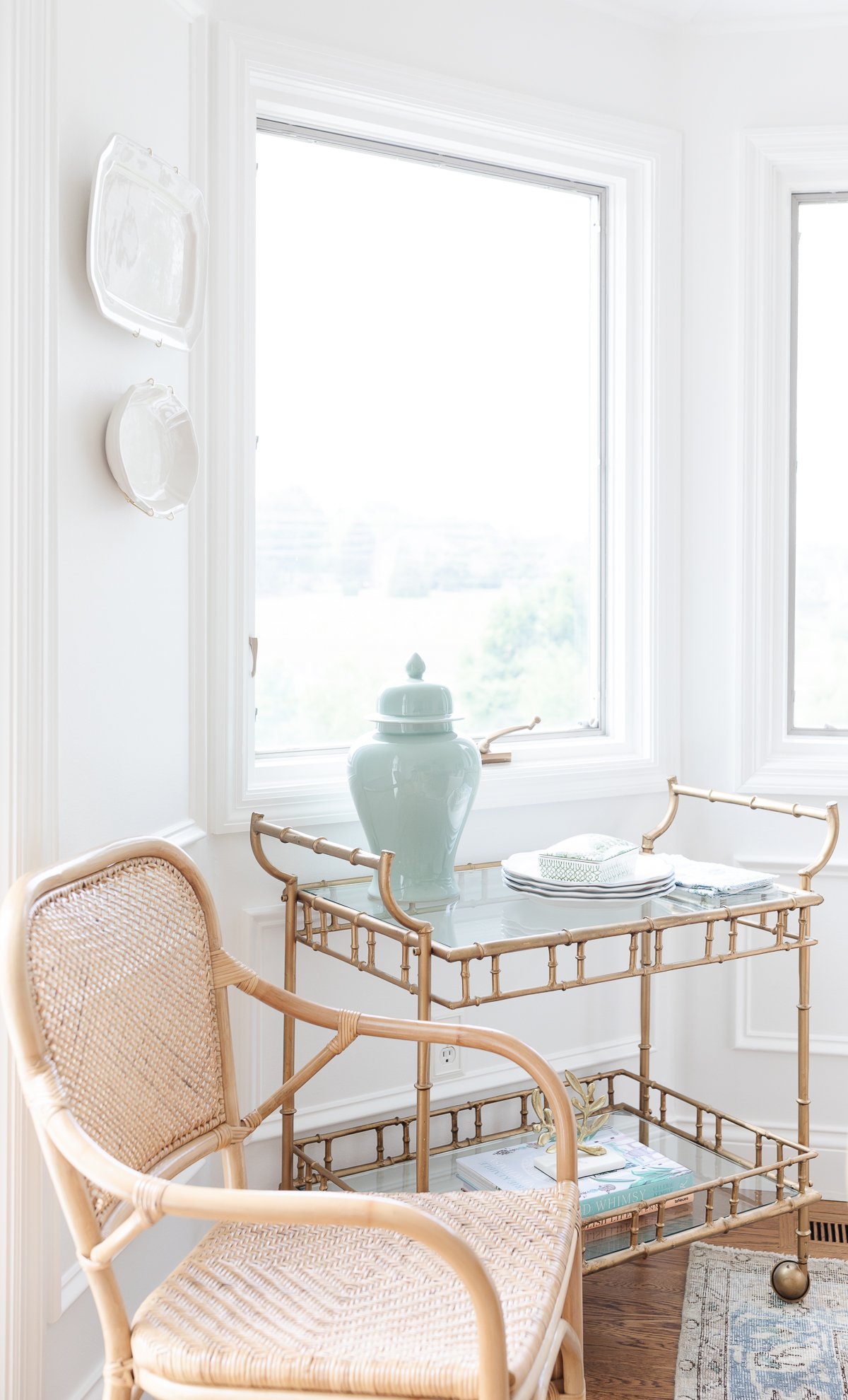 A gold bar cart with a rattan dining chair next to it.