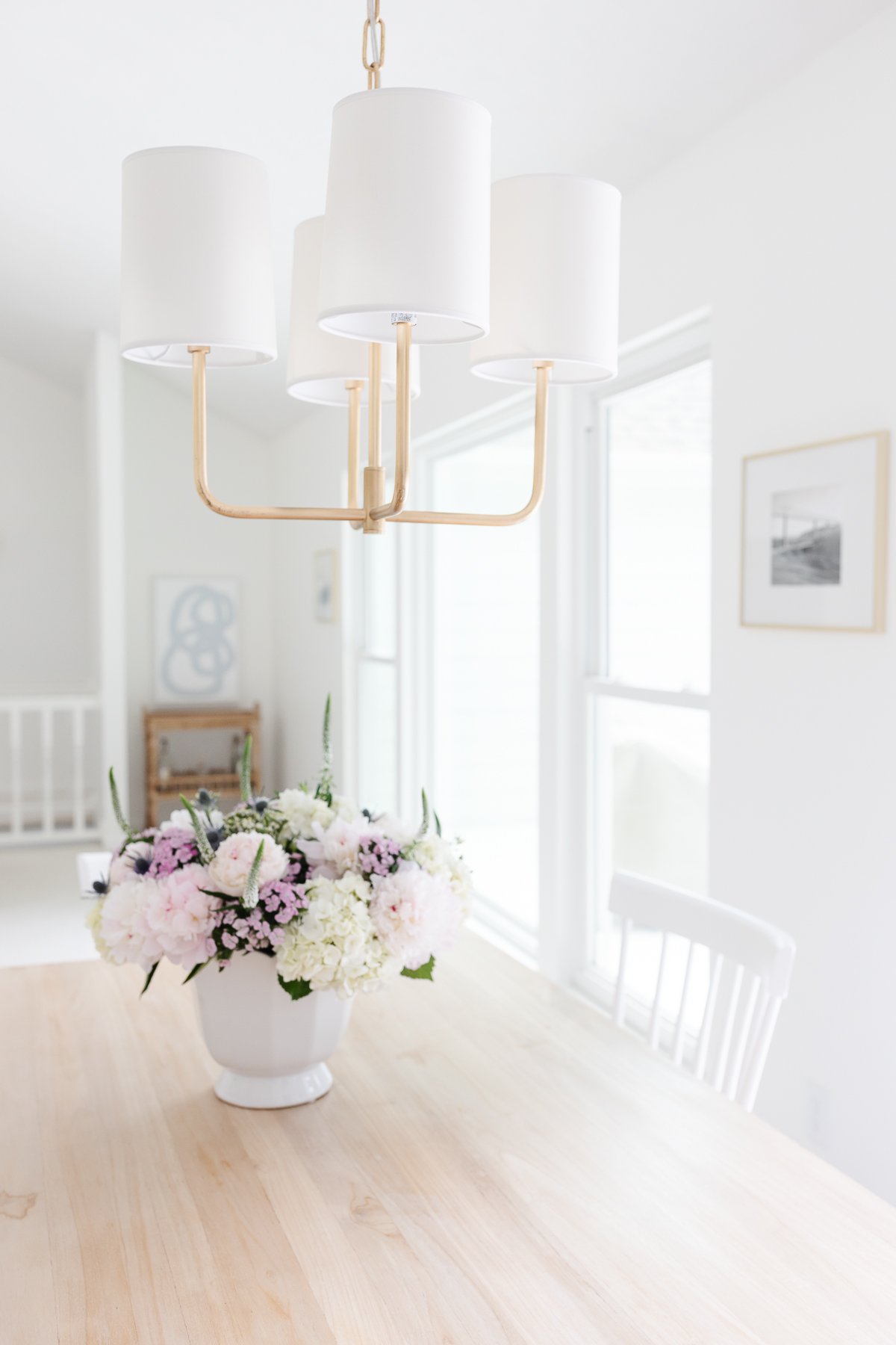 A chandelier hanging from a ceiling over a teak table adorned with flowers.