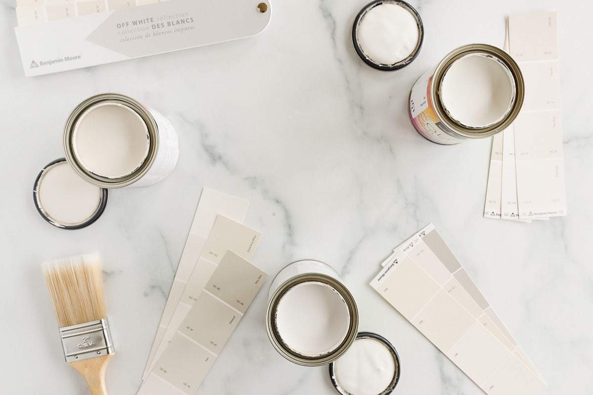 A marble countertop with paint swatches and small cans of open cream paint colors.