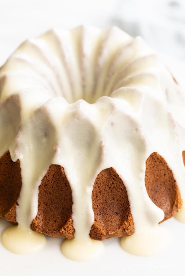 A frosted pumpkin bundt cake on a white marble surface.