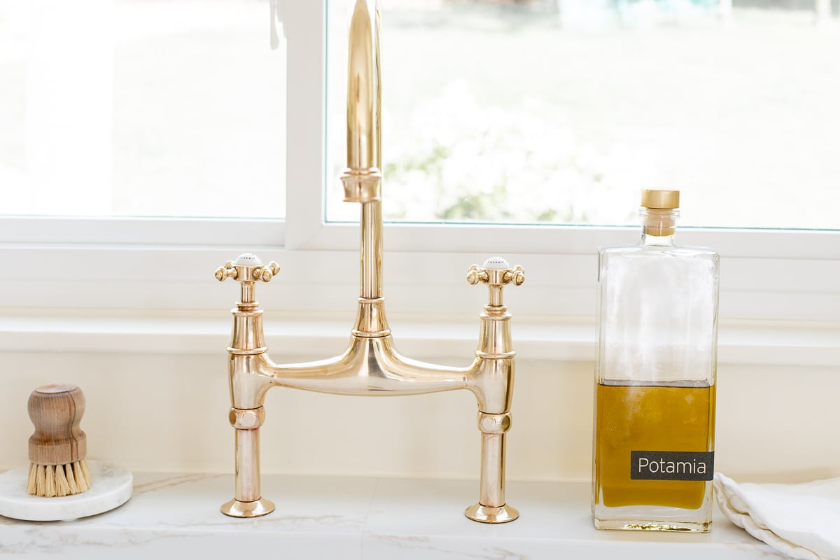 An unlacquered brass kitchen faucet in a white kitchen.