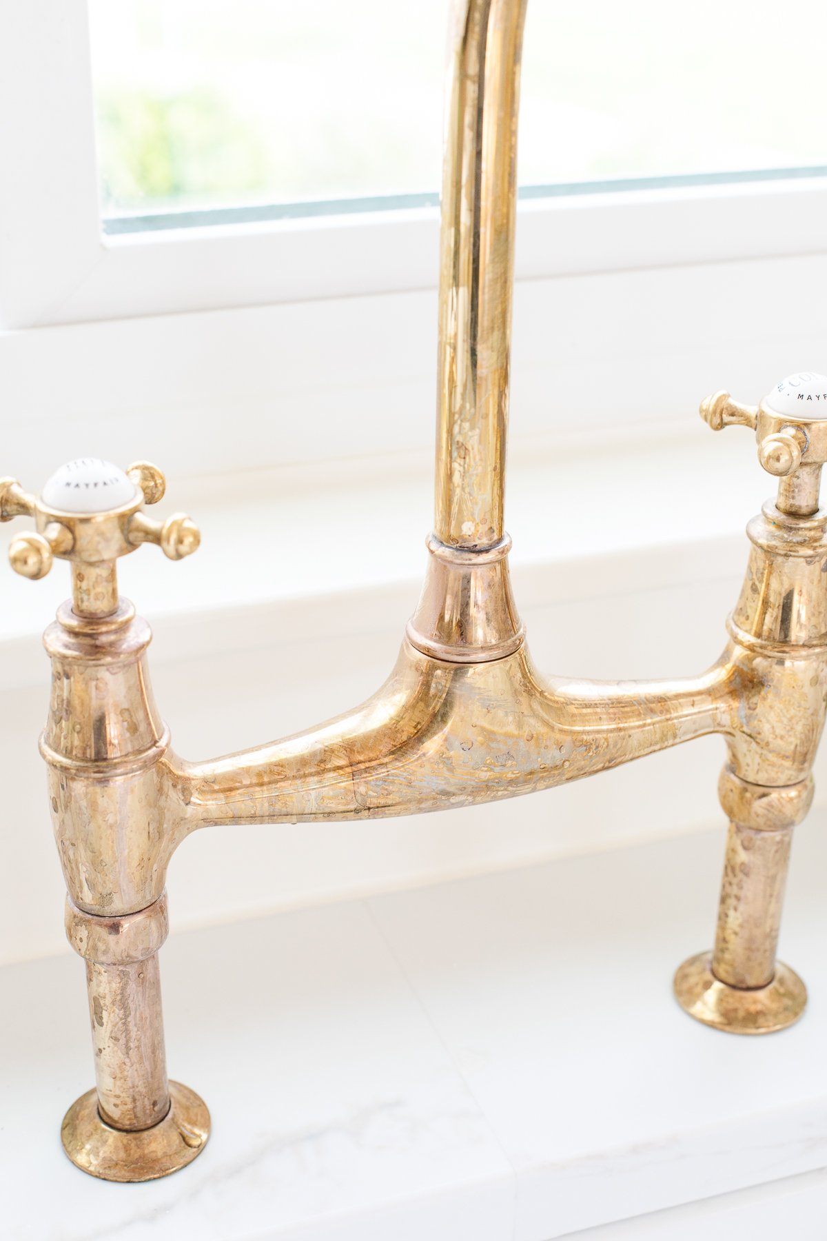 An unlacquered brass kitchen faucet in a white kitchen.