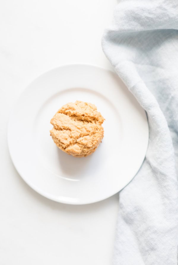 A single scone rests on a white plate beside a light blue cloth, reminiscent of the simplicity found in flourless peanut butter cookies.