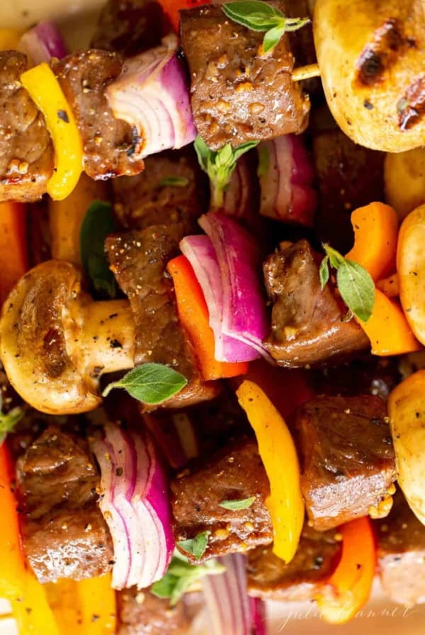 A close up image of steak kabobs on a white platter.