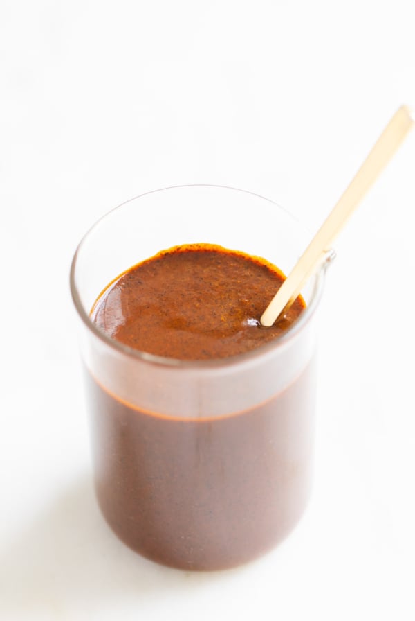 A small clear glass jar filled with enchilada sauce on a white countertop.