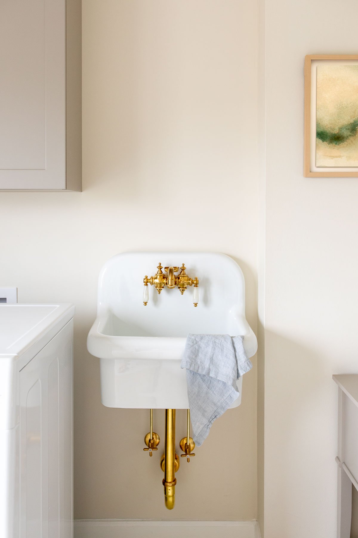 A white ceramic wall mounted sink with brass hardware.