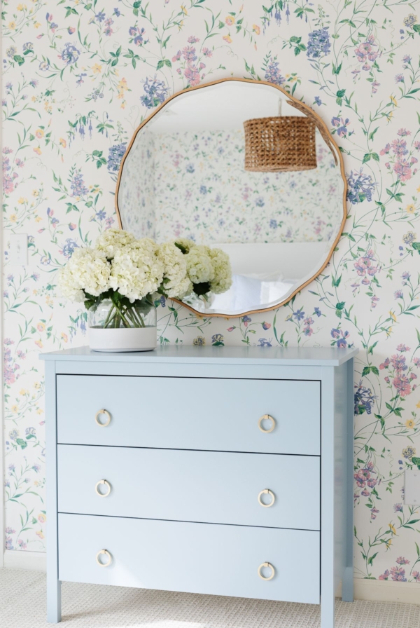 A bedroom with floral wallpaper and a dresser painted in a slate Blue color