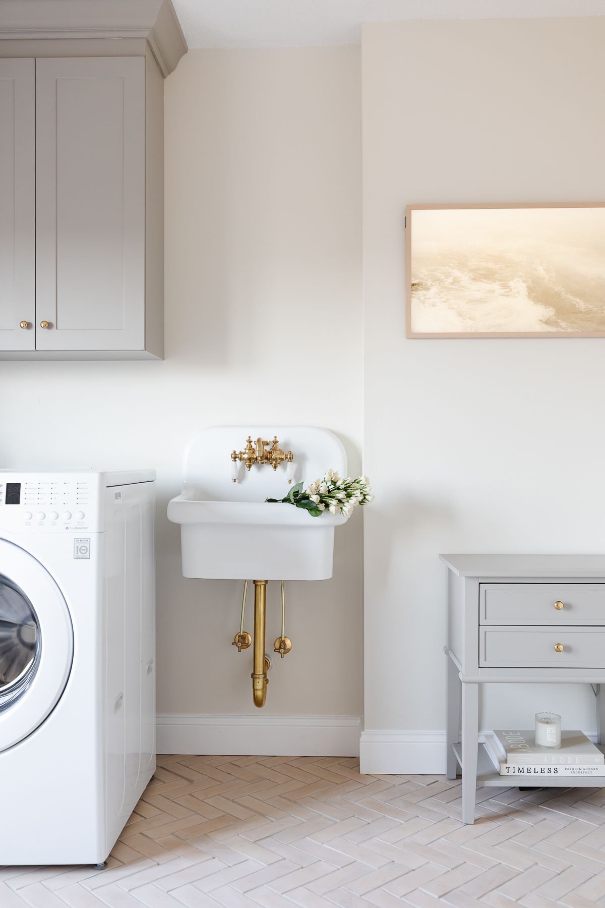 A laundry room with greige cabinets, a wall sink and herringbone floor.