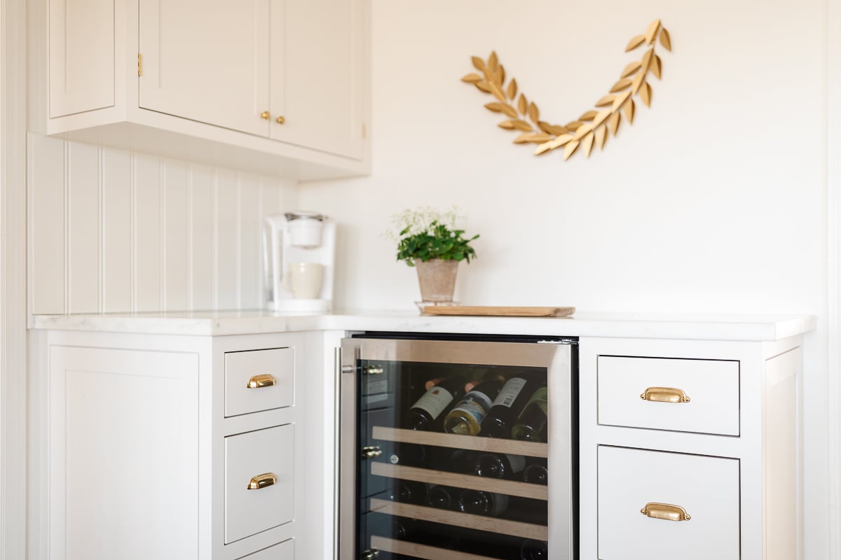 A bar in a cream kitchen with a wine refrigerator. 