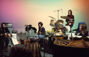 a large soundstage with colourful lights. The Beatles sit at their instruments in front of it