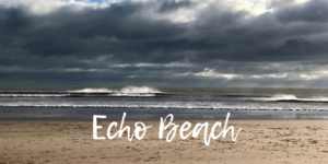 A sunlit English beach in winter. There are large clouds on the horizon and wind-whipped white caps on the waves. White text on the sand reads "Echo Beach"