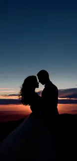 Silhouette of a couple embracing at sunset with a dark blue sky.