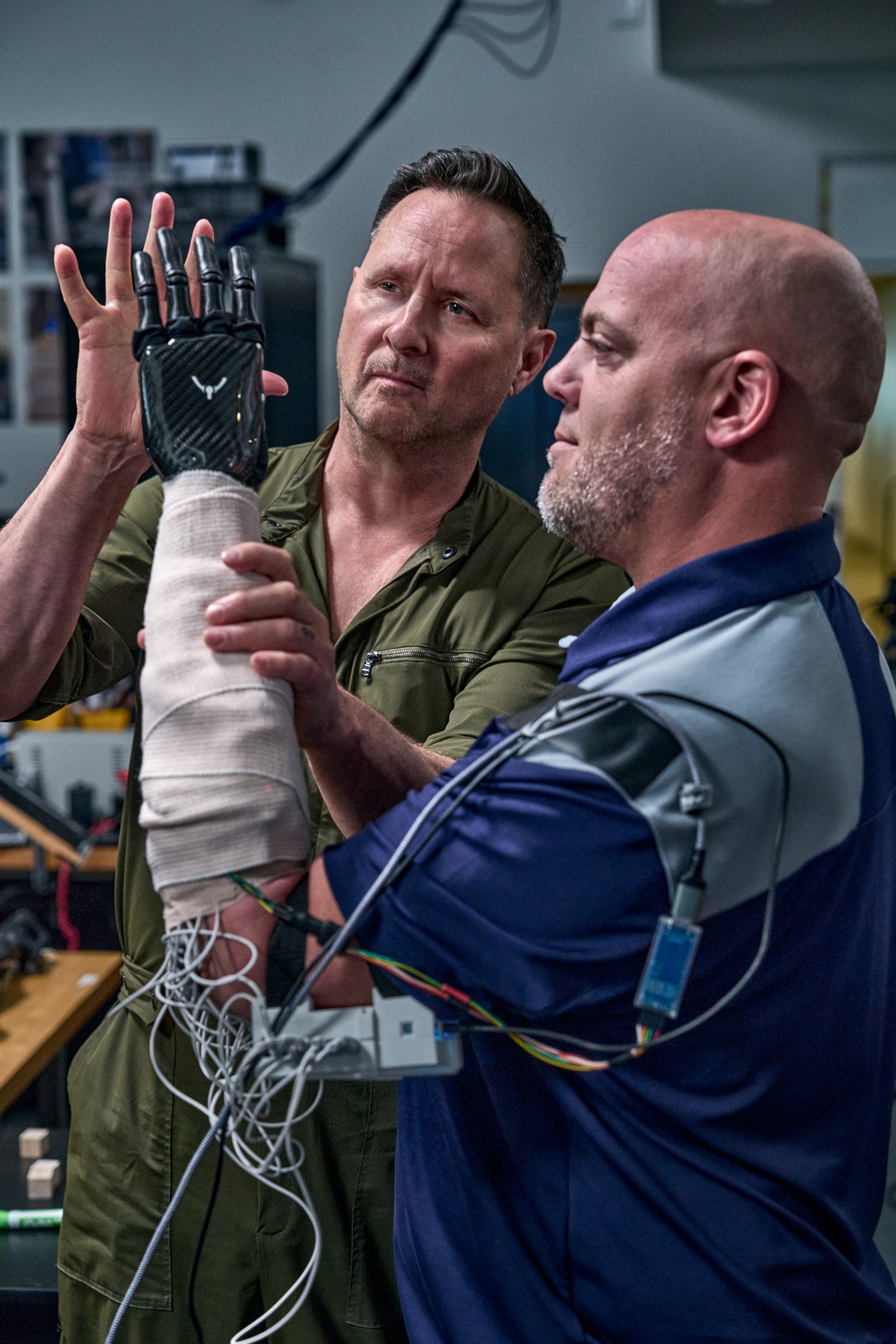 A person with a prosthetic arm that is wired up is reaching for the hand of another person.