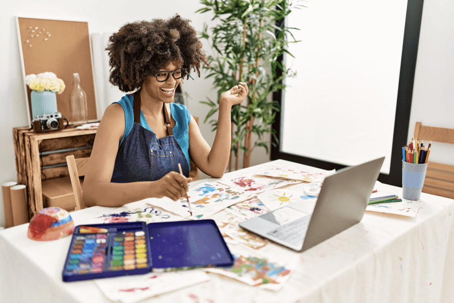 photo of woman painting while using laptop