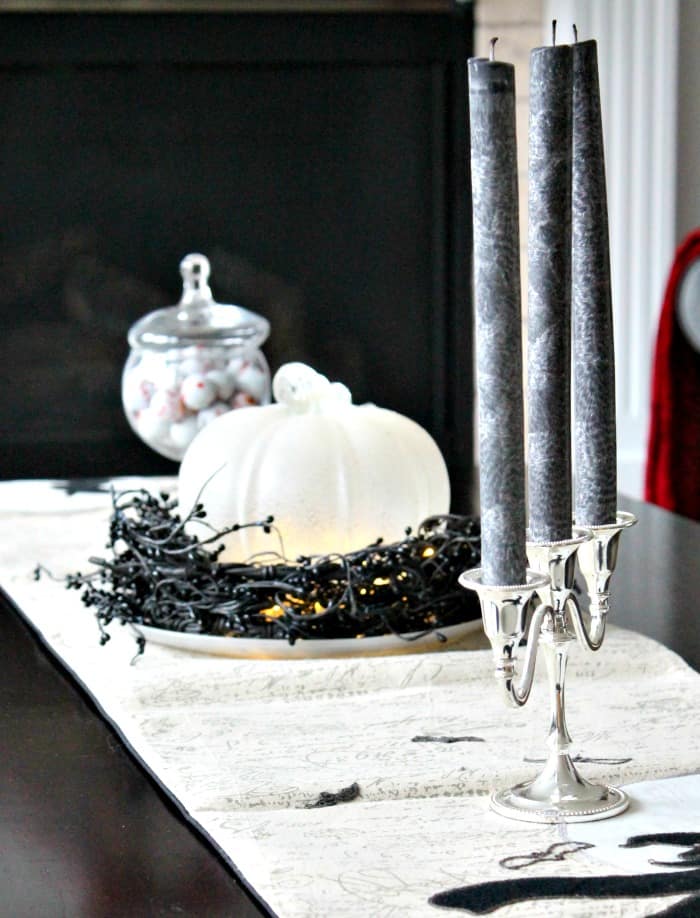 A coffee table decorated for Halloween with elegant silver candlestick, black candles, a white pumpkin, witch table runner and crystal candy jar.