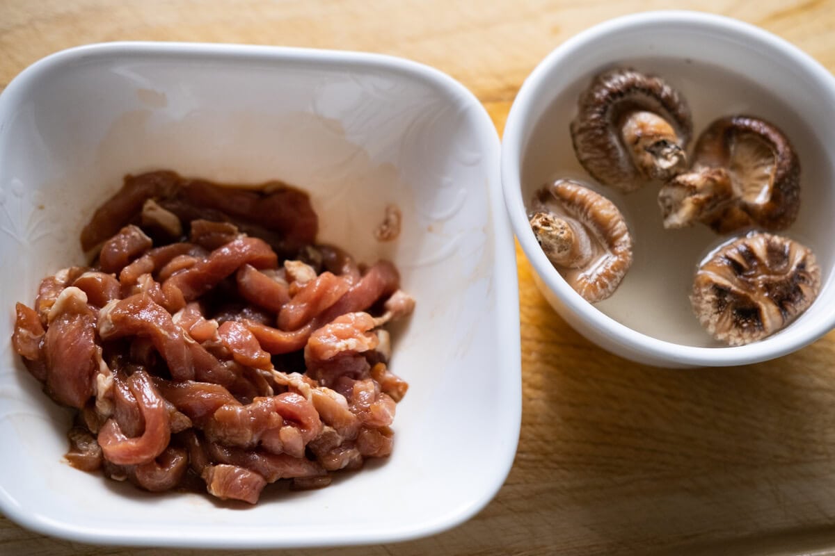 Marinated pork in a bowl and dried shiitake mushrooms in a bowl of water.