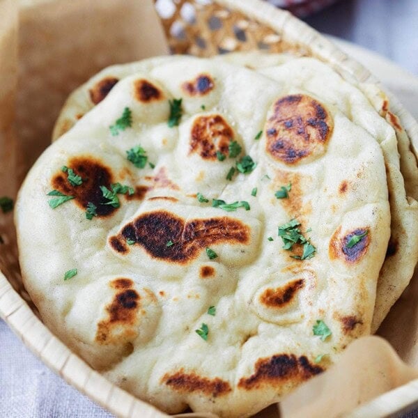 Fluffy and chewy naan with brown bubbly blisters in a bread basket.