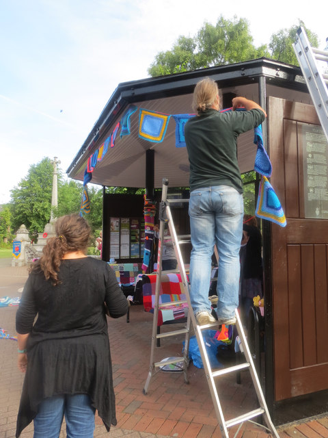 Putting up the yarn fringe round the roof of Tring's Bus Shelter