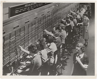 Black and white photo of women working at a telephone switchboard.