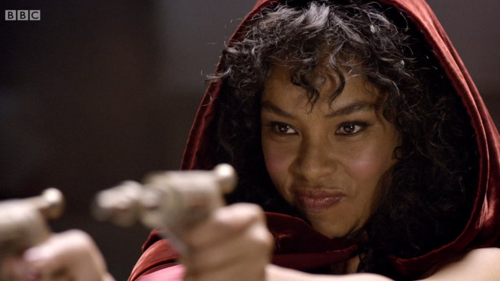 Sophie Okonedo wearing a red cloak and brandishing two laser pistols.