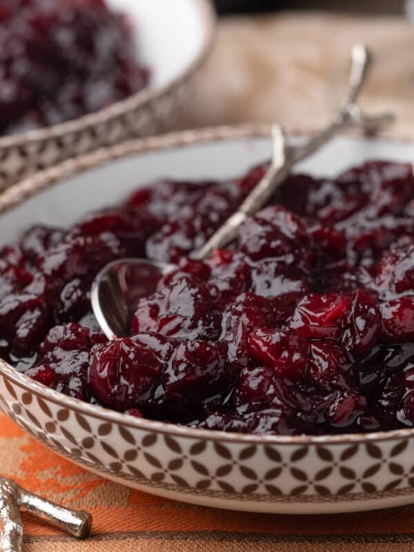 port cranberry sauce in a brown and white patterned bowl with a silver branch motif spoon on an orange damask napkin