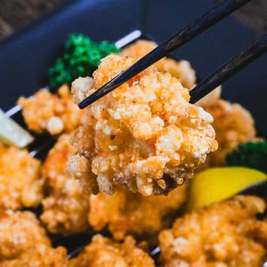 a piece of lemon karaage held with black chopsticks