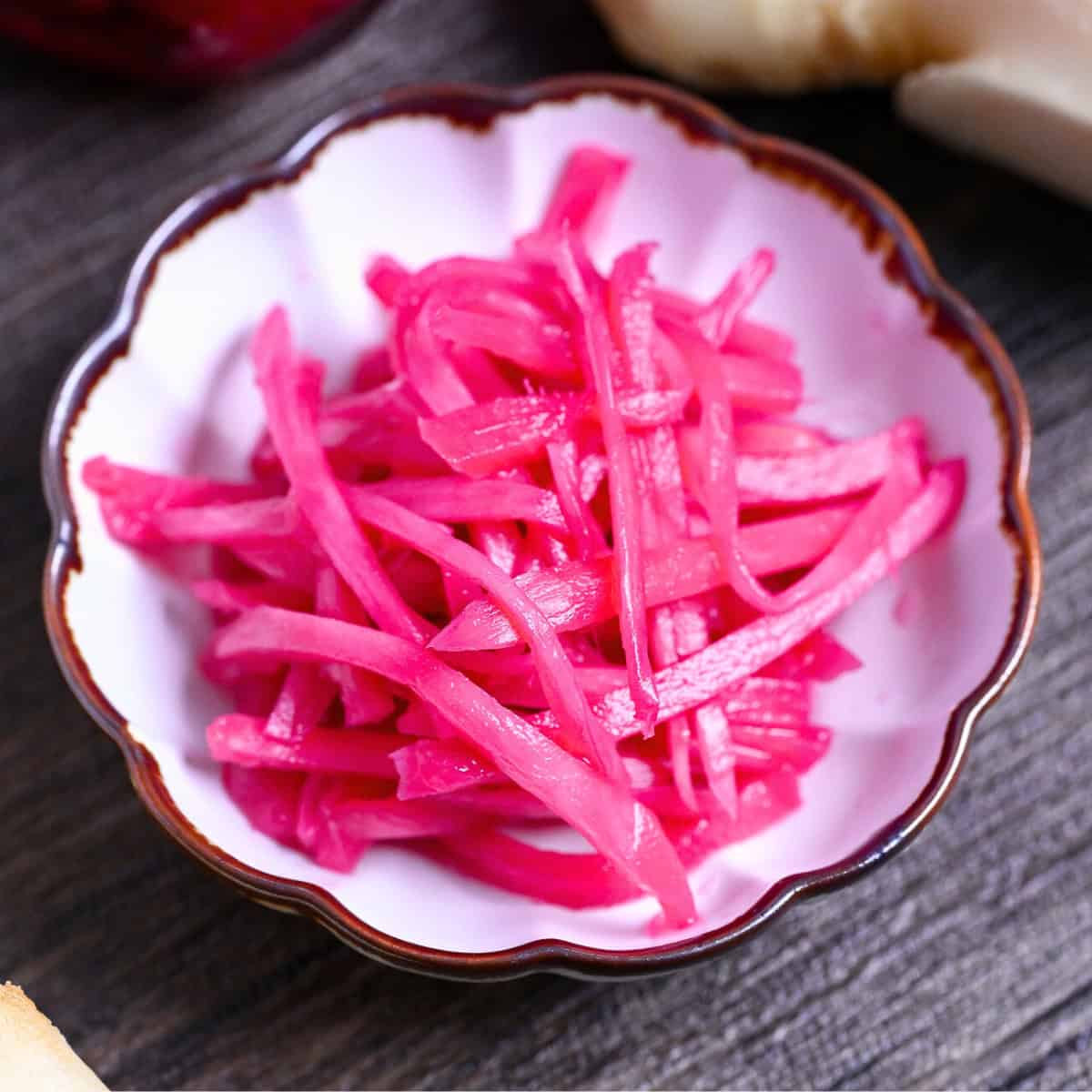 Homemade Japanese red pickled ginger (benishoga) in a white fluted bowl with brown edges