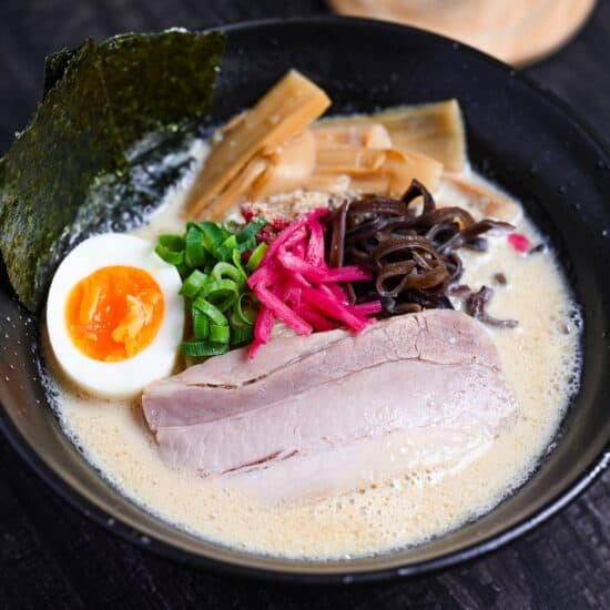 easy shortcut tonkotsu-style ramen topped with pork chashu, ramen egg and shredded vegetables in a black bowl on black wood-effect background